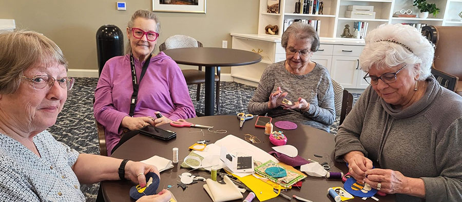 Four women sitting at table with scissors and glue, residents working on crafts together.