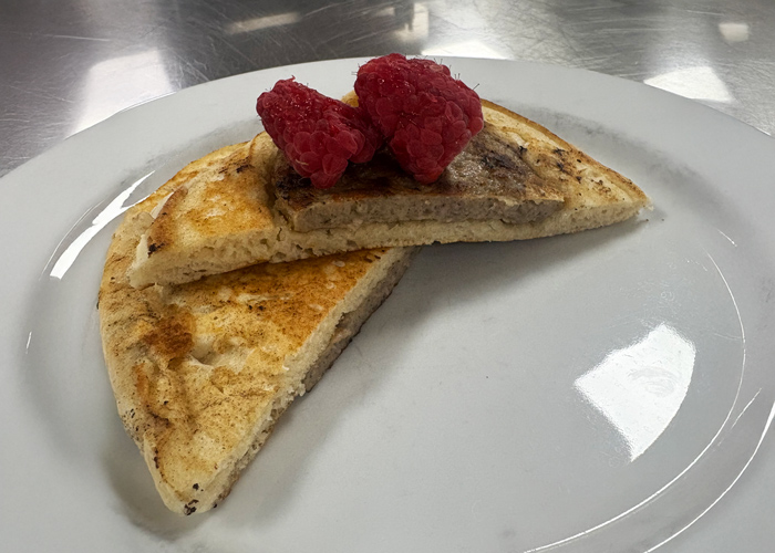 Two slices of a sausage-stuffed pancake topped with fresh raspberries, served on a white plate with a silver background.
