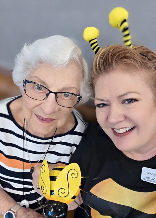 Senior woman and staff member dressed in bee-themed outfits, smiling together during a themed community event