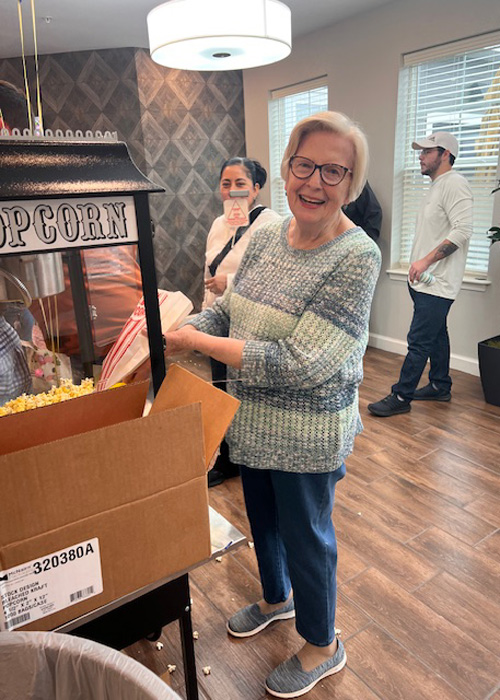 Senior woman smiling while scooping fresh popcorn at a popcorn cart during a fun social gathering in the community