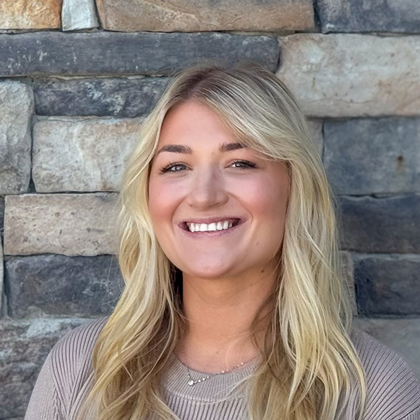 Sage Westerfield, Memory Care Director at The Rushwood Senior Living, smiling in front of a stone wall while wearing a light taupe ribbed top.