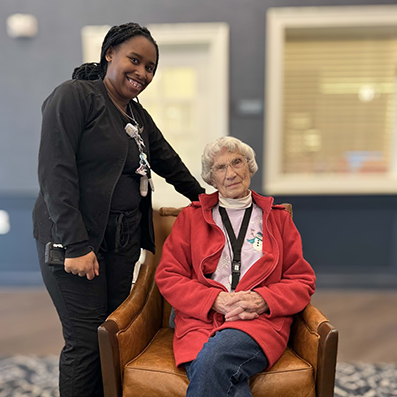 A team member and seated senior woman smile together at The Rushwood.