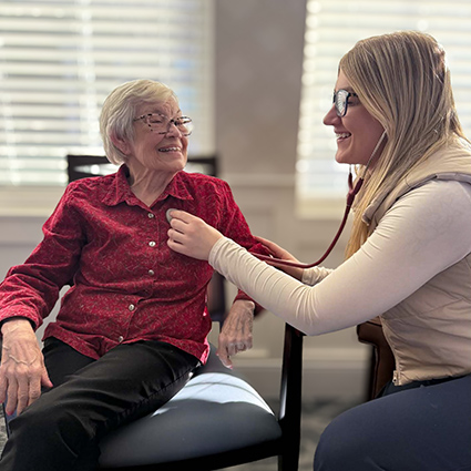 A senior woman smiles while having a wellness checkup at The Rushwood Senior Living.