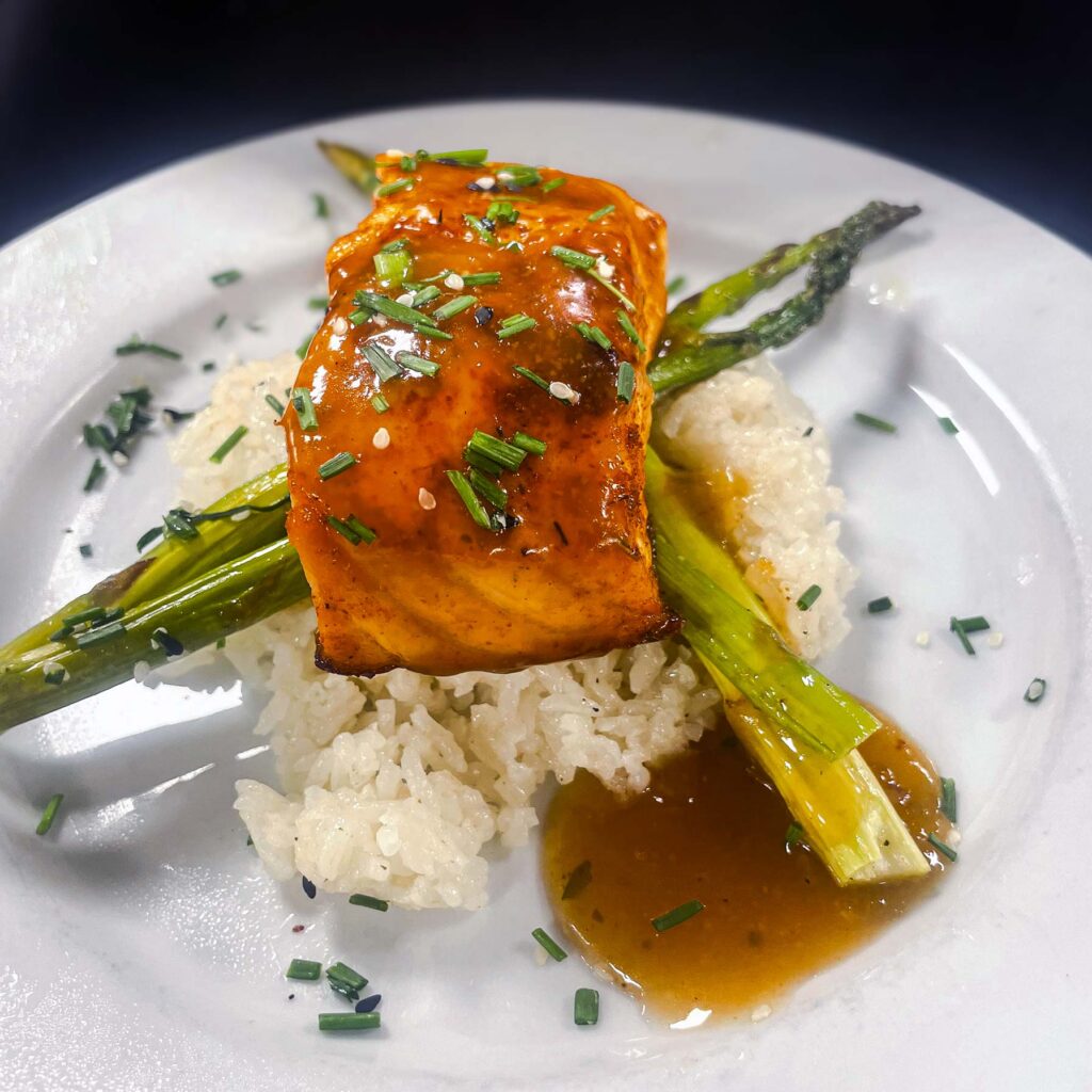 Chef-prepared and plated salmon dish featuring rice, fresh asparagus and drizzled with sauce, at The Rushwood Senior Living.