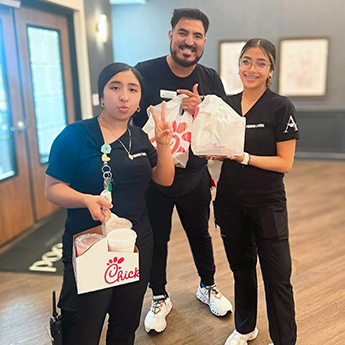 Three team members smile, holding to-go bags from a local restaurant.