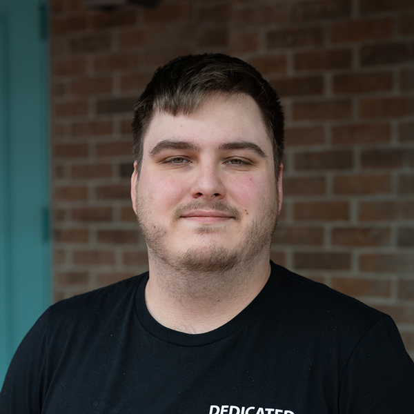 Chris Harding, Culinary Director at The Rushwood Senior Living, posing in a professional headshot, wearing a black shirt, with a softly blurred brick background.