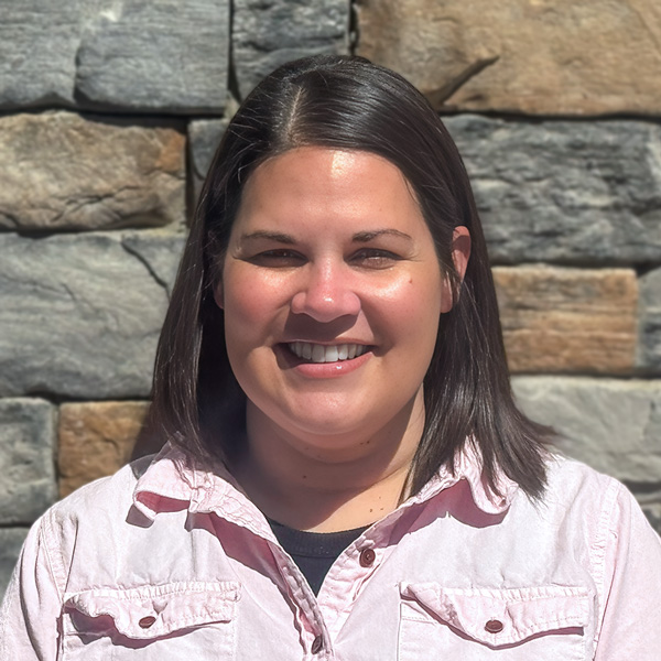 Daysha Johnston, Operations Coordinator at The Rushwood Senior Living, smiling in a professional headshot, wearing a light pink button-down shirt, standing in front of a stone wall background.