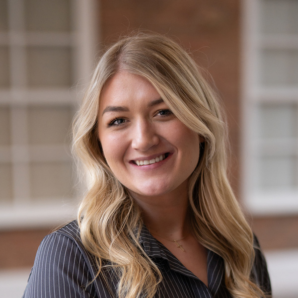 Sage Westerfield, Memory Care Director at The Rushwood Senior Living, smiling in a professional headshot, wearing a striped blouse, with a softly blurred outdoor background featuring brick and window details.