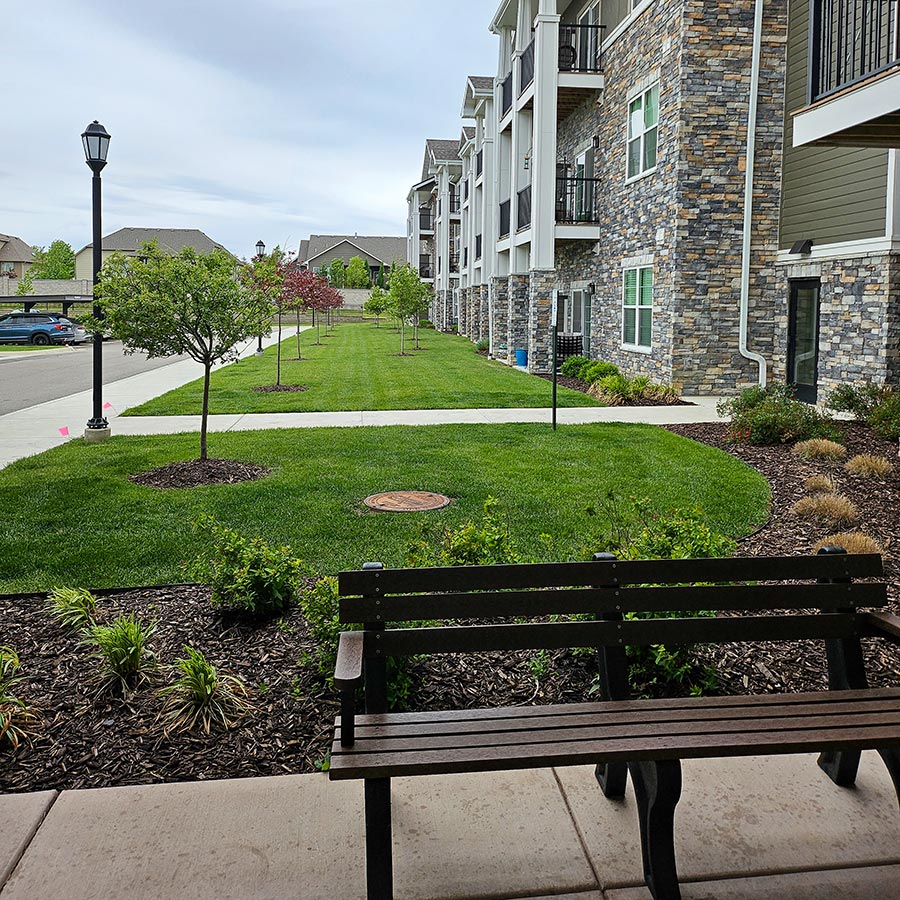 A bench rests beside landscaped mulch beds at The Rushwood Senior Living.