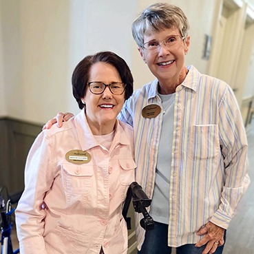 Two senior residents on the Resident Services team smile brightly at The Rushwood Senior Living.